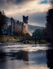 Castillo medieval en ruinas en un dia nublado, junto a un rio y  un puente