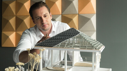 Closeup image of handsome caucasian engineer face inspects roof material while looking at building carefully. Project manager pointing pencil at building roof. Business design concept. Manipulator..