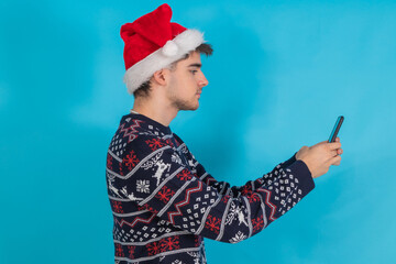 isolated young man in christmas clothes and santa claus hat with mobile phone or smartphone