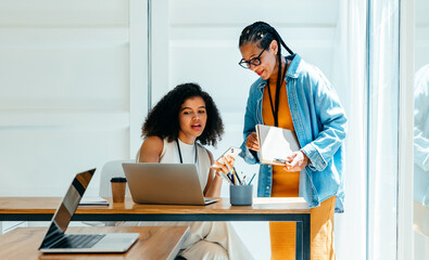 Two businesswomen collaborating with digital technology in a stylish, modern work environment