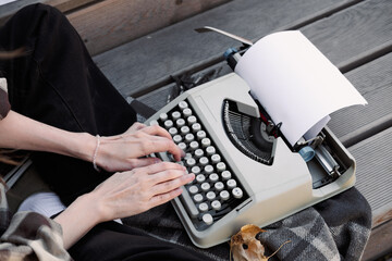 hands of a woman writer on the keyboard of a typewriter on the background of a wooden floor, copy space