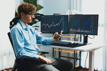 Young investor stock trader looking on smartphone, analyzing dynamic financial exchange investment on two laptop screens background in current market graph in real time at modern office. Gusher.