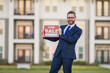 © Volodymyr - Real estate agent hold house sale sign. Real estate sale or property investment concept. Buying new home. Handsome real estate agent in suit showing the house for sale.