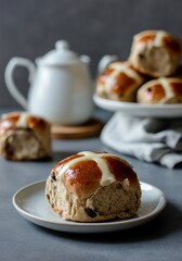 Freshly baked hot cross buns on plate with teapot in background.