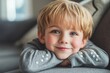 © StockUp - Close-up of a cheerful young boy with blond hair leaning on a soft couch, looking content.