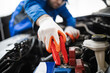 © zphoto83 - A mechanic using jumper cables to start a car battery in a workshop during daytime