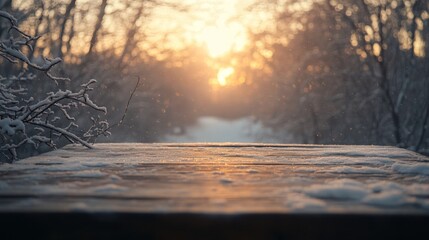 Leinwandbilder - A wooden surface dusted with snow overlooks a serene pathway as the sun sets behind the trees, casting warm light through the winter scene. The atmosphere feels peaceful and quiet at dusk.