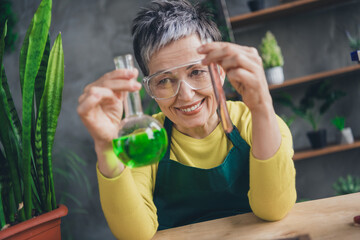 Photo of nice elderly lady create fertilizer wear green apron enjoying gardering indoors home business workplace