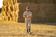© Volodymyr - Farmer In Wheat Field After Harvest Examining Hay. Crops After Harvesting. Farm Lifestyle. Barn, Hay Rolled Bales. Hay On Farm. Livestock Farming. Agriculture business farm concept.