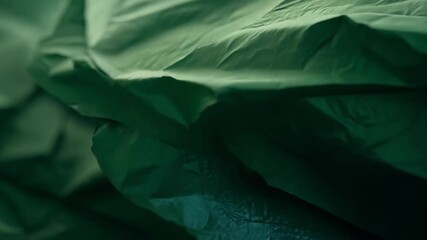 Poster - A close-up showcases crumpled green paper, allowing its unique texture and subtle shadows to emerge under soft, warm lighting that highlights its folds.