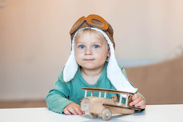 a handsome little boy of 2 years old in a pilot's hat is playing with a wooden airplane and a logist