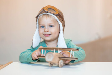 a handsome little boy of 2 years old in a pilot's hat is playing with a wooden airplane and a logist