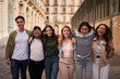 © CarlosBarquero - Happy group of diverse generation z tourism people strolling embracing on streets of tourist city. Cheerful young friends looking smiling at camera walking hugging together enjoying holiday outdoors