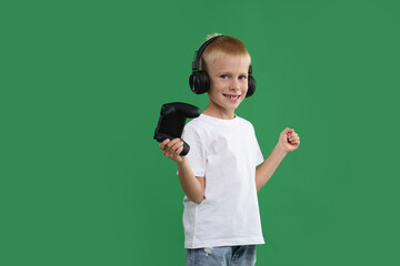 Happy little boy in headphones with controller on green background. Space for text