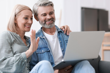 Happy middle aged couple having video chat via laptop on sofa indoors