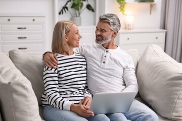 Happy middle aged couple using laptop on sofa at home