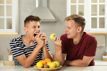 Happy brothers eating apples at table in kitchen