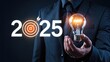 © Vodkaz - Businessman holding a glowing light bulb representing future goals for 2025.