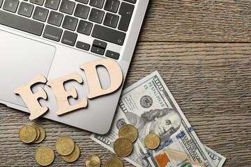 Letters Fed (Federal Reserve System), coins, dollar banknotes and laptop on wooden table, flat lay