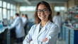© Sajal.savar - A young Woman in White Coat and Glasses Standing in Medical Science Laboratory Team of Specialists in the Background.