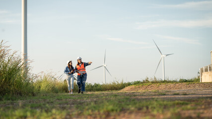 two engineersare walking on a dirt road next to a wind farm. One of them is pointing to a wind turbine