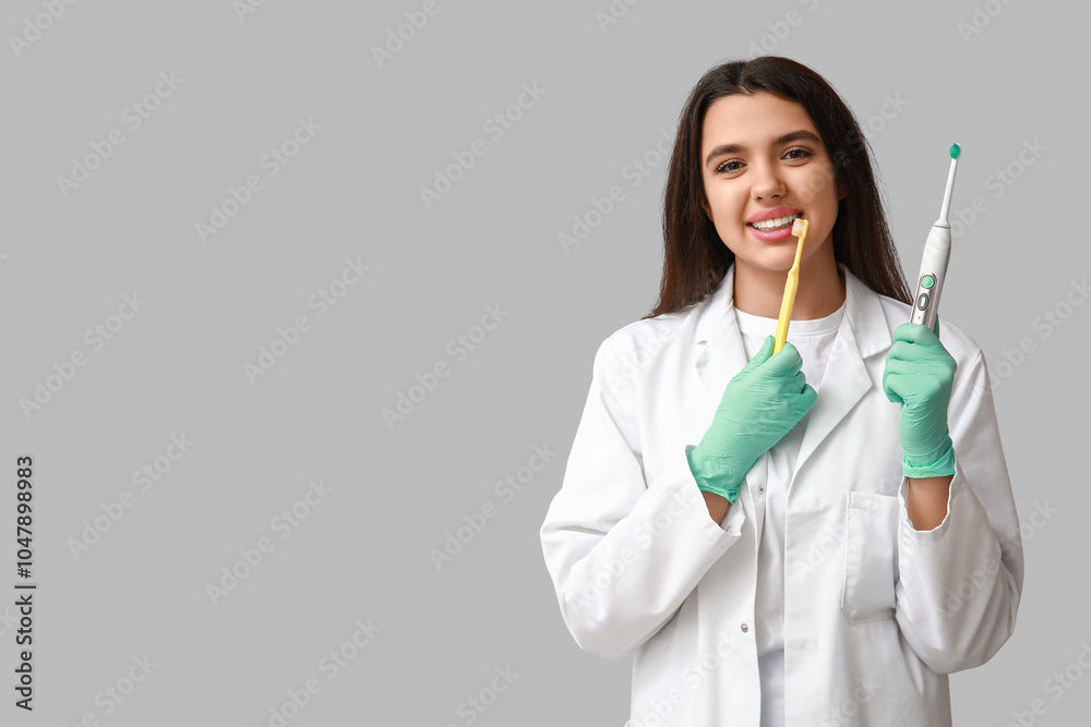 Female dentist with toothbrushes on grey background. World Dentist Day