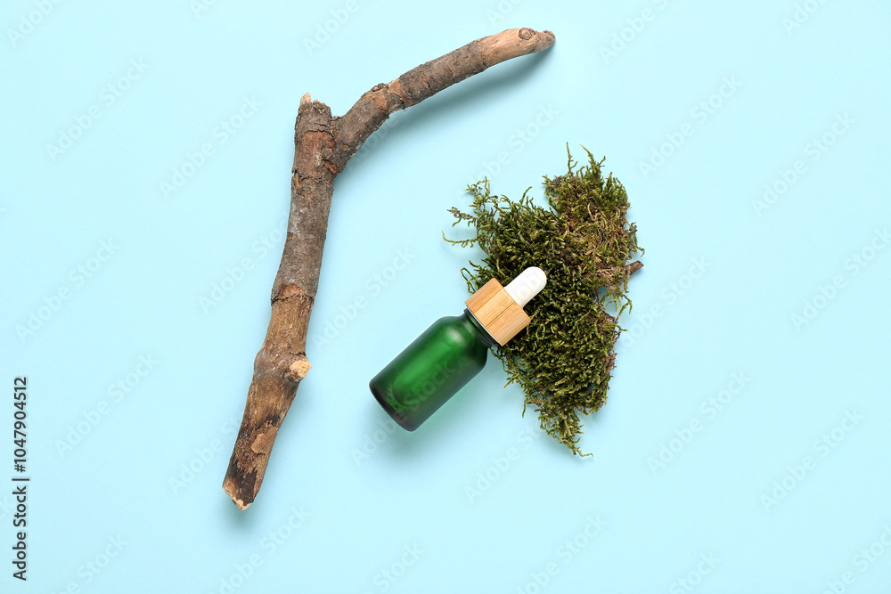 Tree bark, green moss and bottle of essential oil on blue background