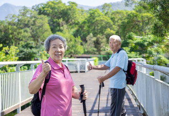 Wall Mural - Happy asian senior couple hiking in the nature and showing thumbs up