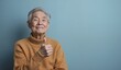 © Yury - Senior Asian Man with Cheerful Expression Giving Thumbs Up Against Blue Background with Copy Space