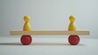 © peerawat - Red and yellow pawn figures positioned on either end of a wooden seesaw, gently tilting as they balance, set against a clean, minimalistic backdrop, illustrating the concept of balance and compromise