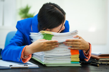 A businesswoman sits at her desk in the office, exhausted and stressed from checking company documents. She suffers from headaches and anxiety due to being overloaded with work and prolonged sitting