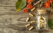 © Who is Santi - Ashwagandha Root Supplement in a Natural Setting: An up-close image of ashwagandha root capsules in a clear glass bottle, accompanied by pieces of ashwagandha root on a rustic wooden surface