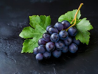 A bunch of grapes with green leaves on a black surface