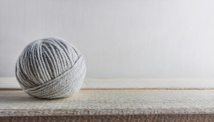 Ball of woolen knitting thread on wooden table, white wall. Hobby and leisure concept.