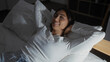 © Krakenimages.com - Young, hispanic woman lying on a bed in a cozy bedroom, smiling and looking relaxed in an indoor home setting