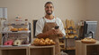 © Krakenimages.com - Young man with beard holding phone standing in bakery shop with pastries and bread in the background