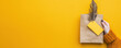 © Worawut - Eco friendly packaging held in hands against vibrant yellow background, showcasing sustainability and creativity. brown paper bag features yellow tag and decorative feather, emphasizing unique touch