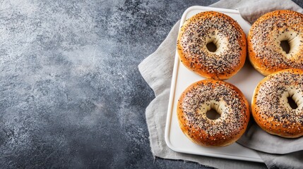Poster - Four fresh baked bagels with poppy seeds on a white tray, on a linen cloth.
