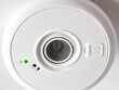 © Vectplus - Detailed close-up of a white smoke detector with a green indicator light and a mesh grille, highlighting its design and function