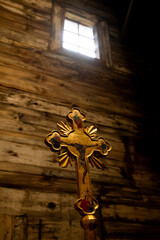 a photograph of an old gold cross in a wooden church in the with light coming from a window above