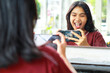 © M Alfan Setyawan - pretty asian woman standing in front of mirror of cafe playing game online using mobile phone screaming with excitement