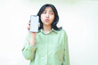 © M Alfan Setyawan - thoughtful asian woman holding smartphone showing white empty screen wearing green oversized clothes looking away pondering standing isolated background