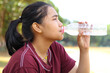 © M Alfan Setyawan - asian woman drinking a bottle of water while sitting under tree in outdoor feels tired and dehidrated