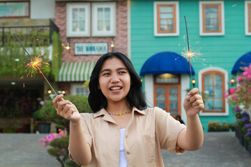 portrait of beautiful happy young asian woman holding sparklers fireworks to celebrate new year eve with garden party standing in outdoor vintage house yard