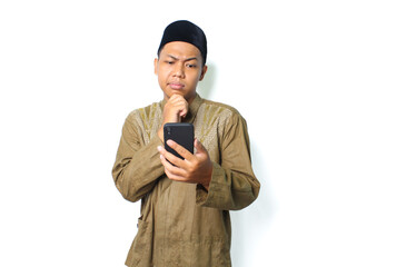 thoughtful asian muslim man holding mobile phone with thouching his chin isolated on white background