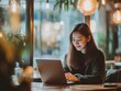 © Bijac - joyful asian woman working on a laptop in a warm, inviting cafe, with soft light filtering through the window, creating a peaceful work environment surrounded by muted colors