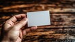 © BloomArt - Hand holding blank white card on wooden surface.