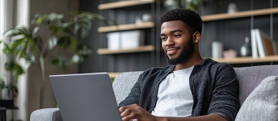 Poster - Smiling young professional using a laptop while sitting on a couch in a contemporary office. with copy space image. Place for adding text or design