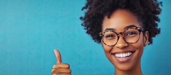 Poster - A beautiful young African American woman wearing glasses is smiling happily against an isolated background looking to the side and giving a thumbs up. with copy space image