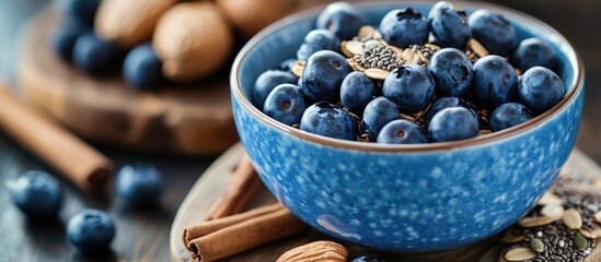 Leinwandbilder - Healthy natural food concept A close up of fresh blueberries in a blue bowl with blurry granola and chia seeds featured in a shallow depth of field On a wooden board there are some almonds cinnamon